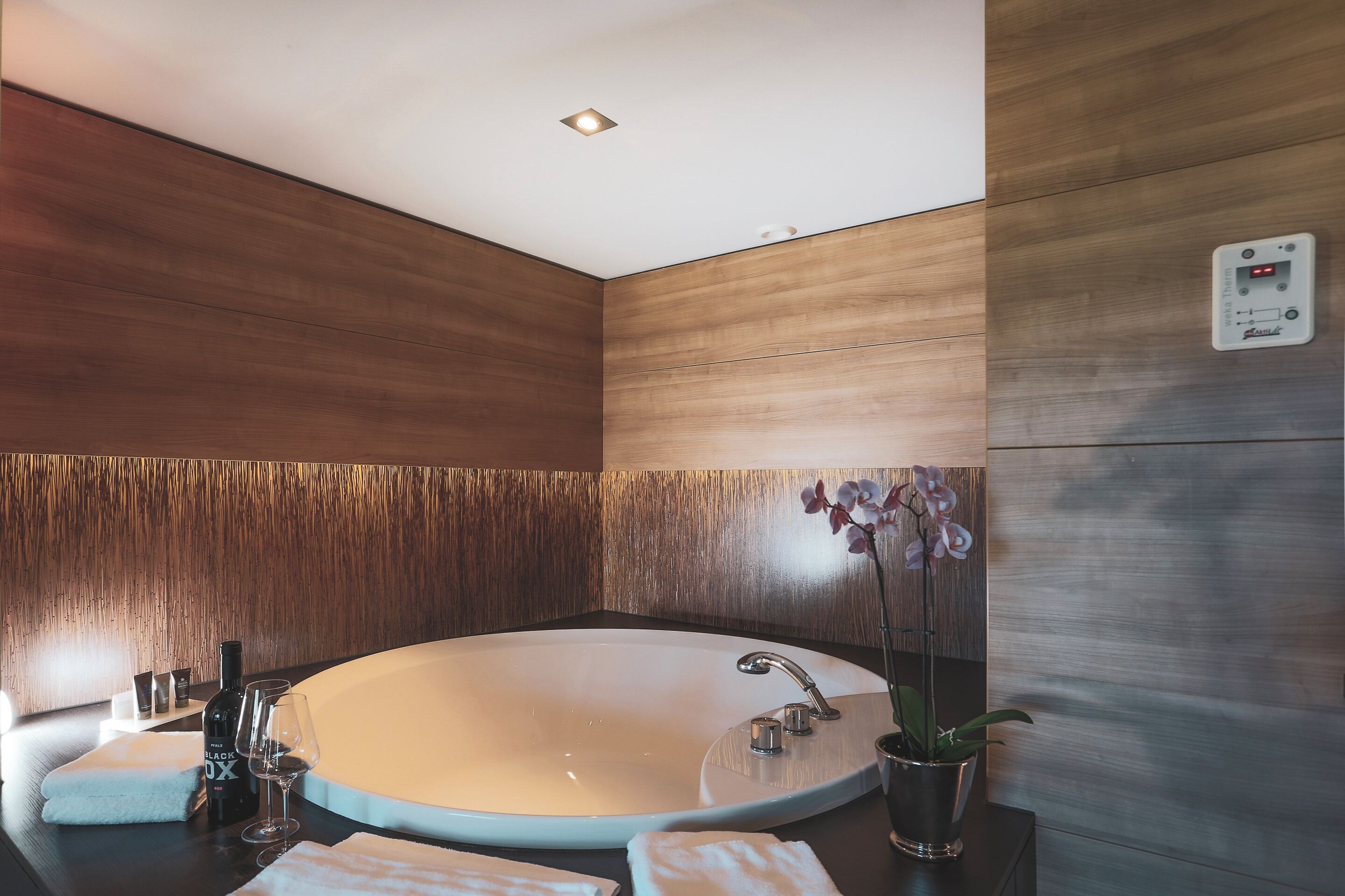 Un baño moderno con una bañera independiente, un calentador de pared y una orquídea en maceta.