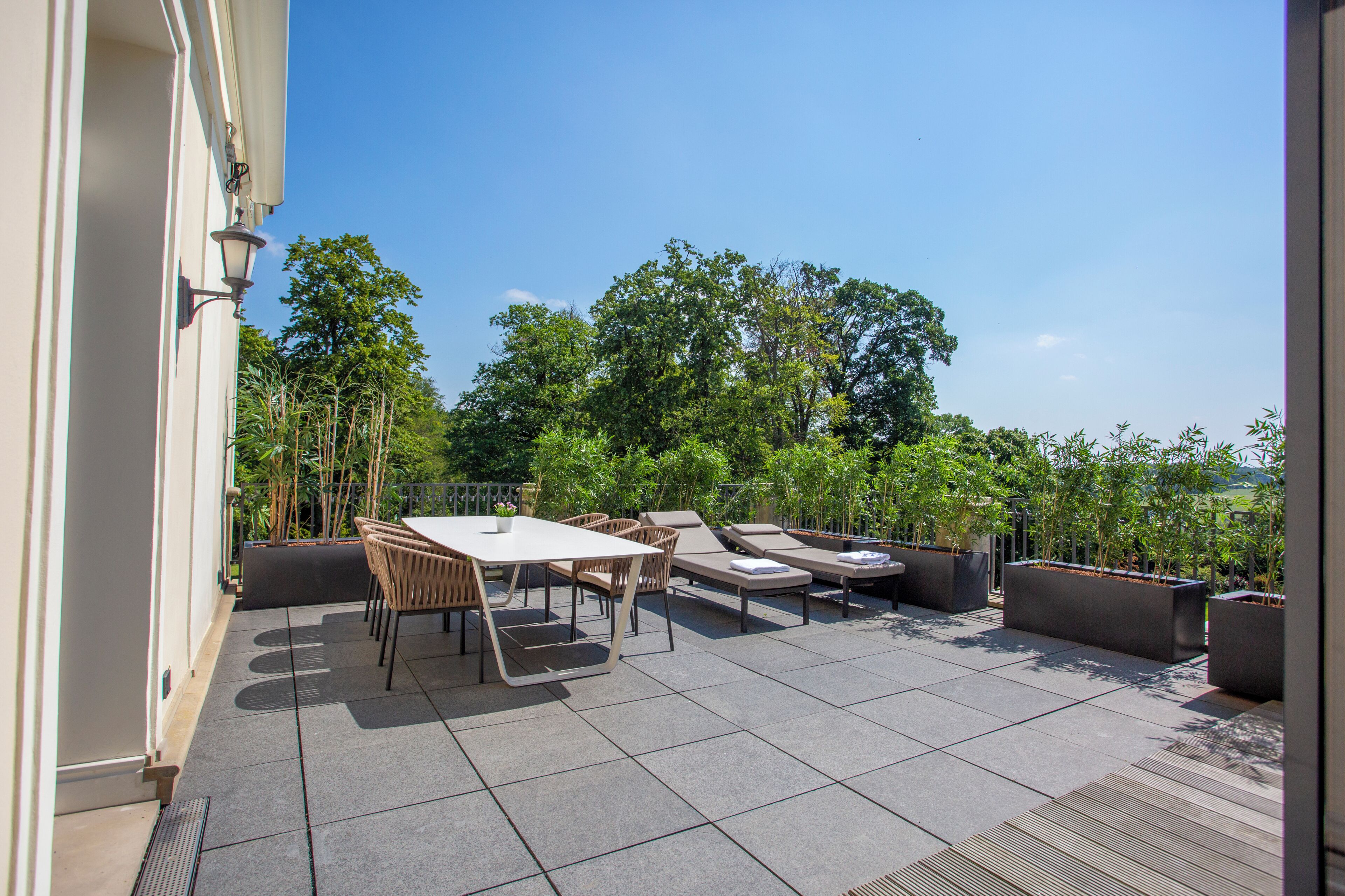 Une terrasse extérieure avec une table et des chaises, des fauteuils de jardin et des plantes en pot.