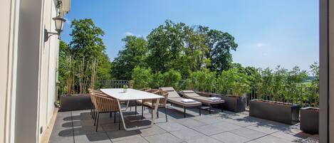 Un patio al aire libre con una mesa y sillas, sillones de descanso y plantas en macetas.