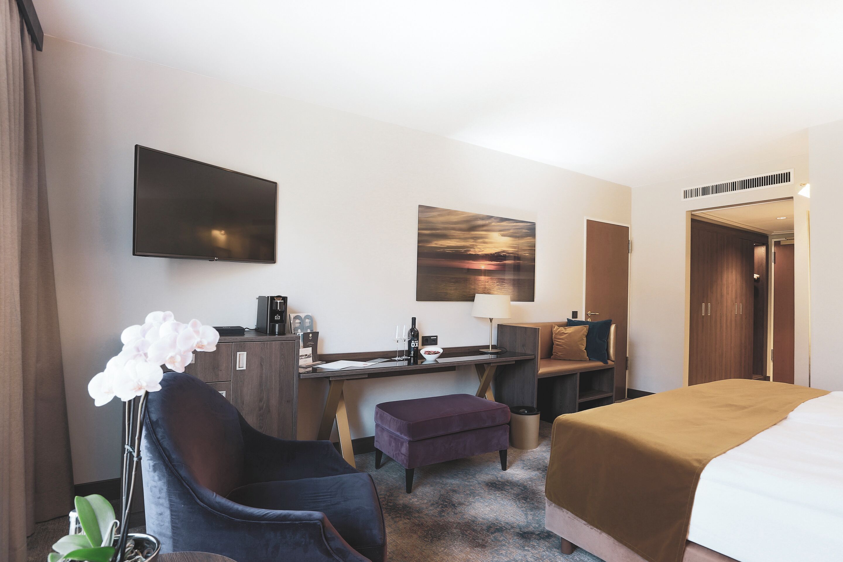 Una camera d'hotel con un letto, una scrivania, una sedia, una televisione, un quadro e un fiore.