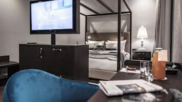 A hotel room with a bed, a TV, a desk, a chair, a bedside table, and a lamp.