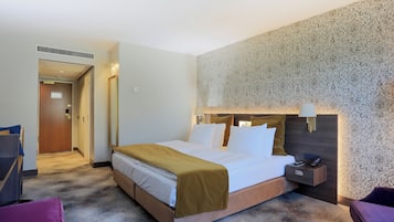 A hotel room with a bed, a bedside table with a lamp, a chair, and a carpeted floor.