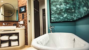 A bathroom with a freestanding bathtub, a mirror, and a television mounted on the wall.