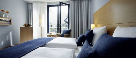 Habitación de hotel con dos camas, vistas al exterior, una mesita con una silla y una ventana con cortinas.