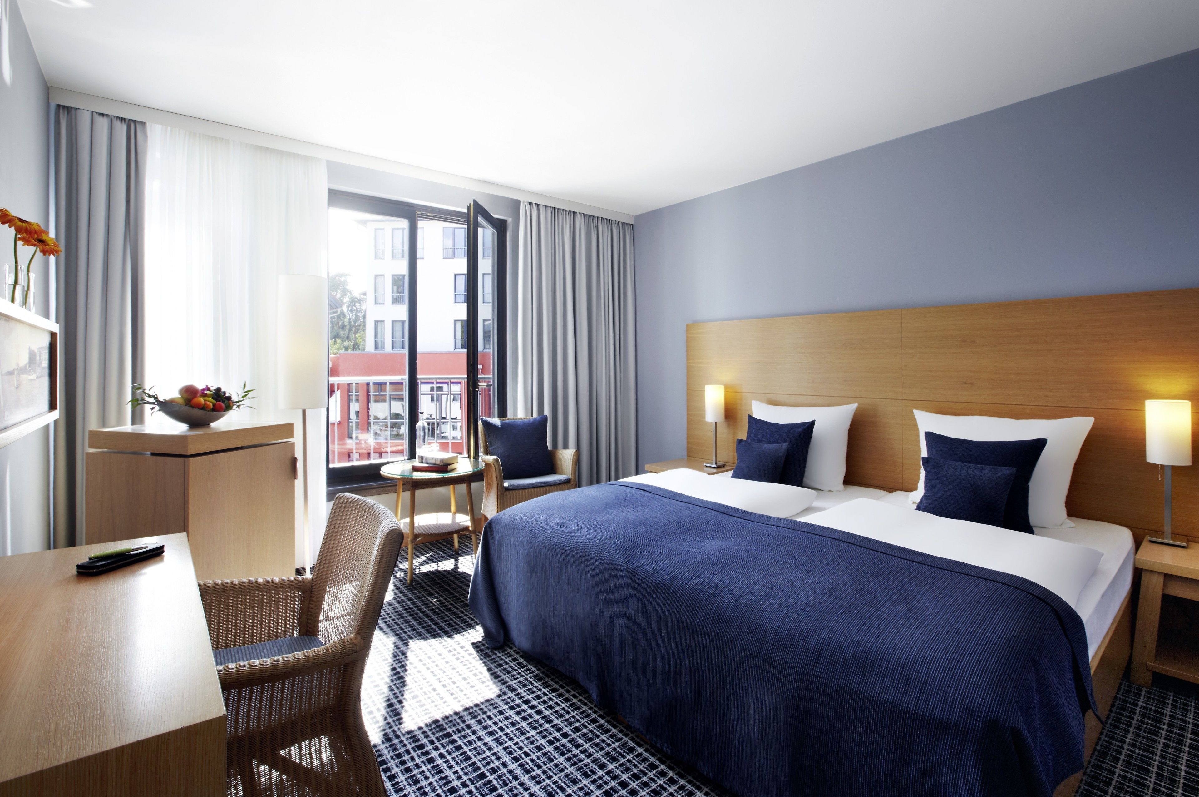 A hotel room with a large bed, a desk, a chair, a small table, and a window with curtains.
