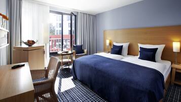 A hotel room with a large bed, a desk, a chair, a small table, and a window with curtains.