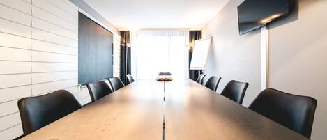 A conference room with a long table, chairs, a TV, and a whiteboard.