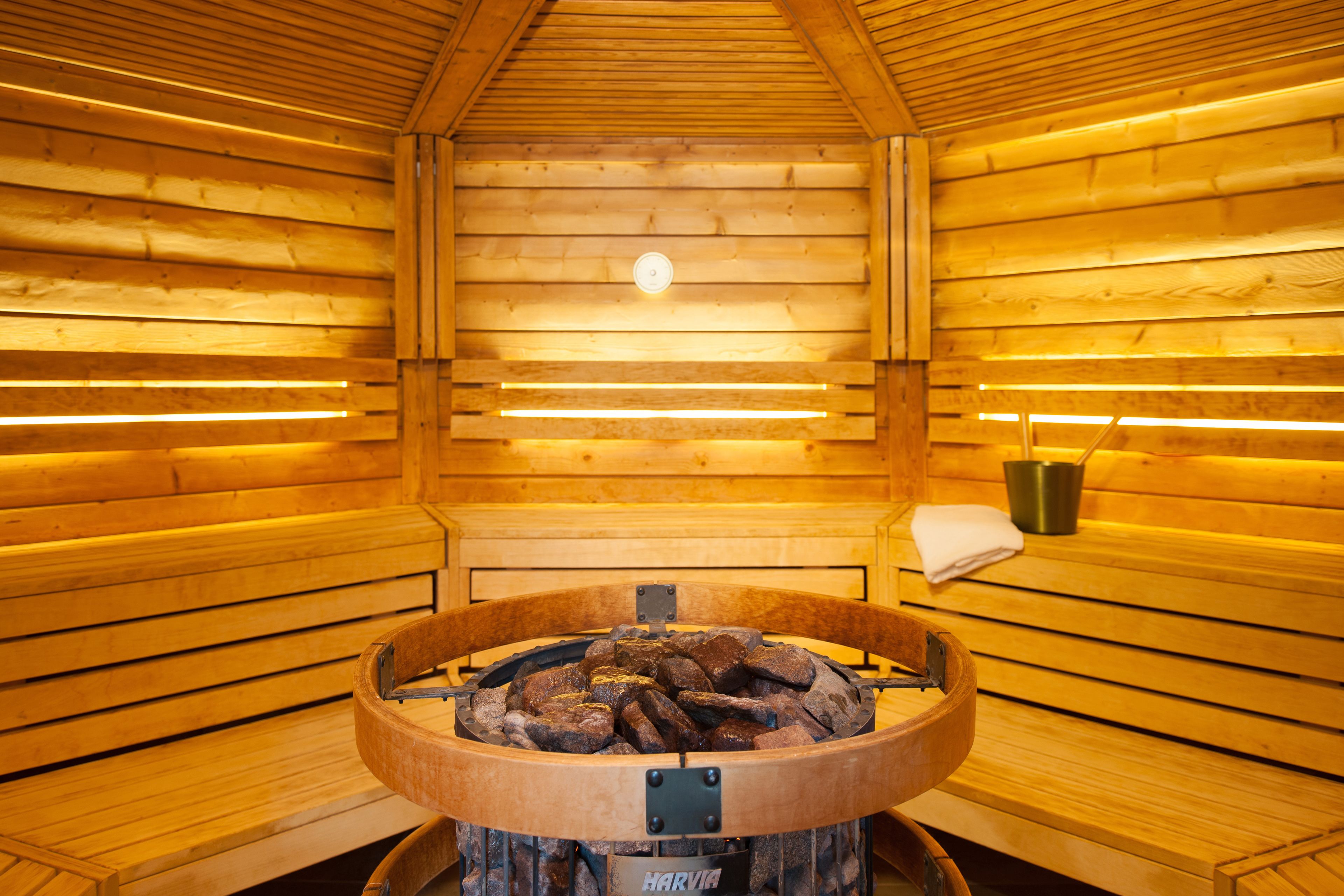 A sauna room with wooden walls, a central fire pit, and benches.