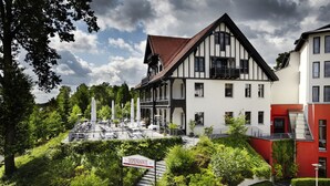A hotel with a traditional European architectural style, featuring a prominent balcony and a staircase leading to the entrance.