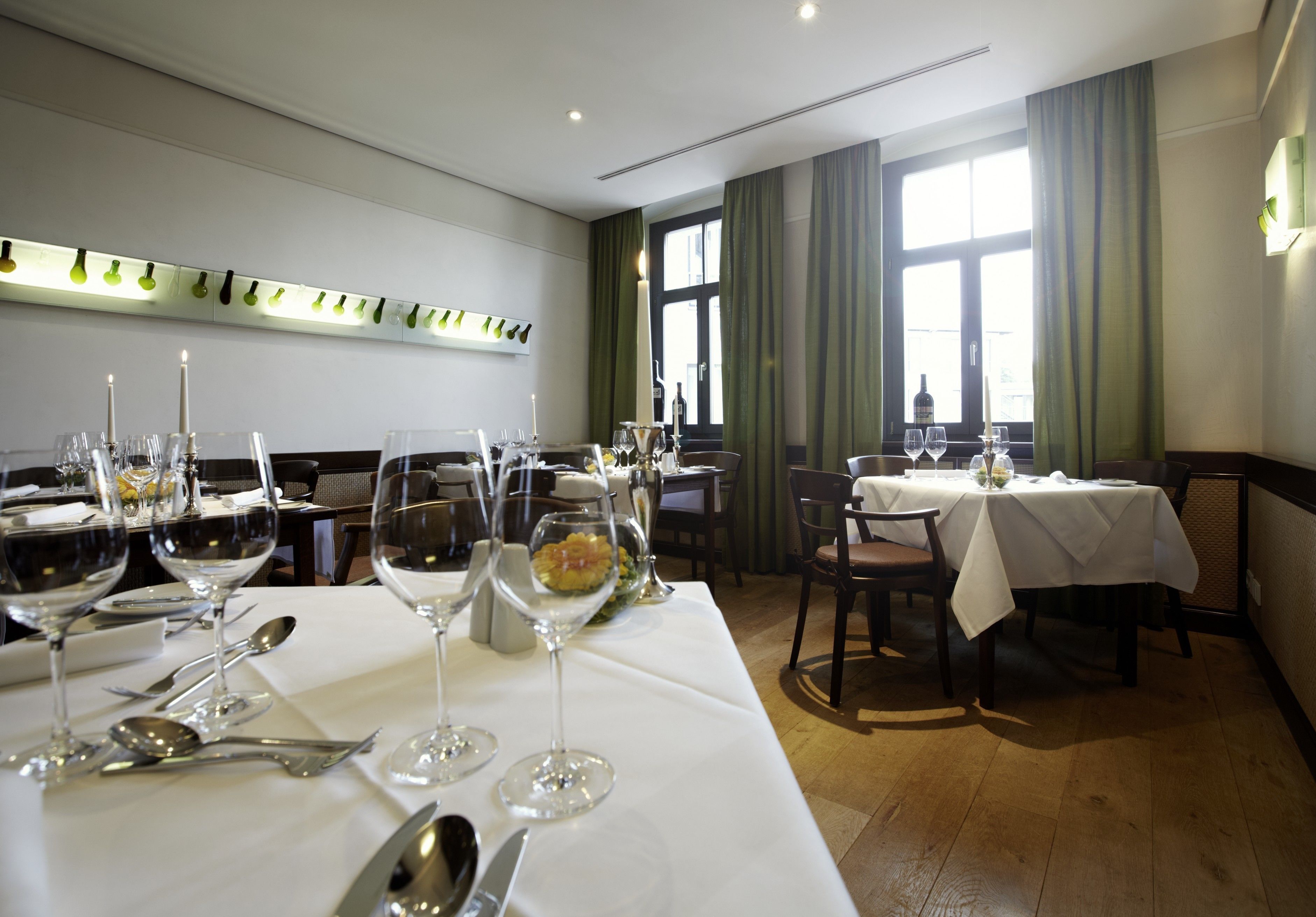 Un restaurant où les tables sont dressées pour le dîner, avec des verres à vin, des couverts et un chandelier servant de décoration centrale.
