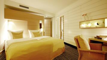 A hotel room with a large bed, a chair, a desk, and a mirror on the wall.