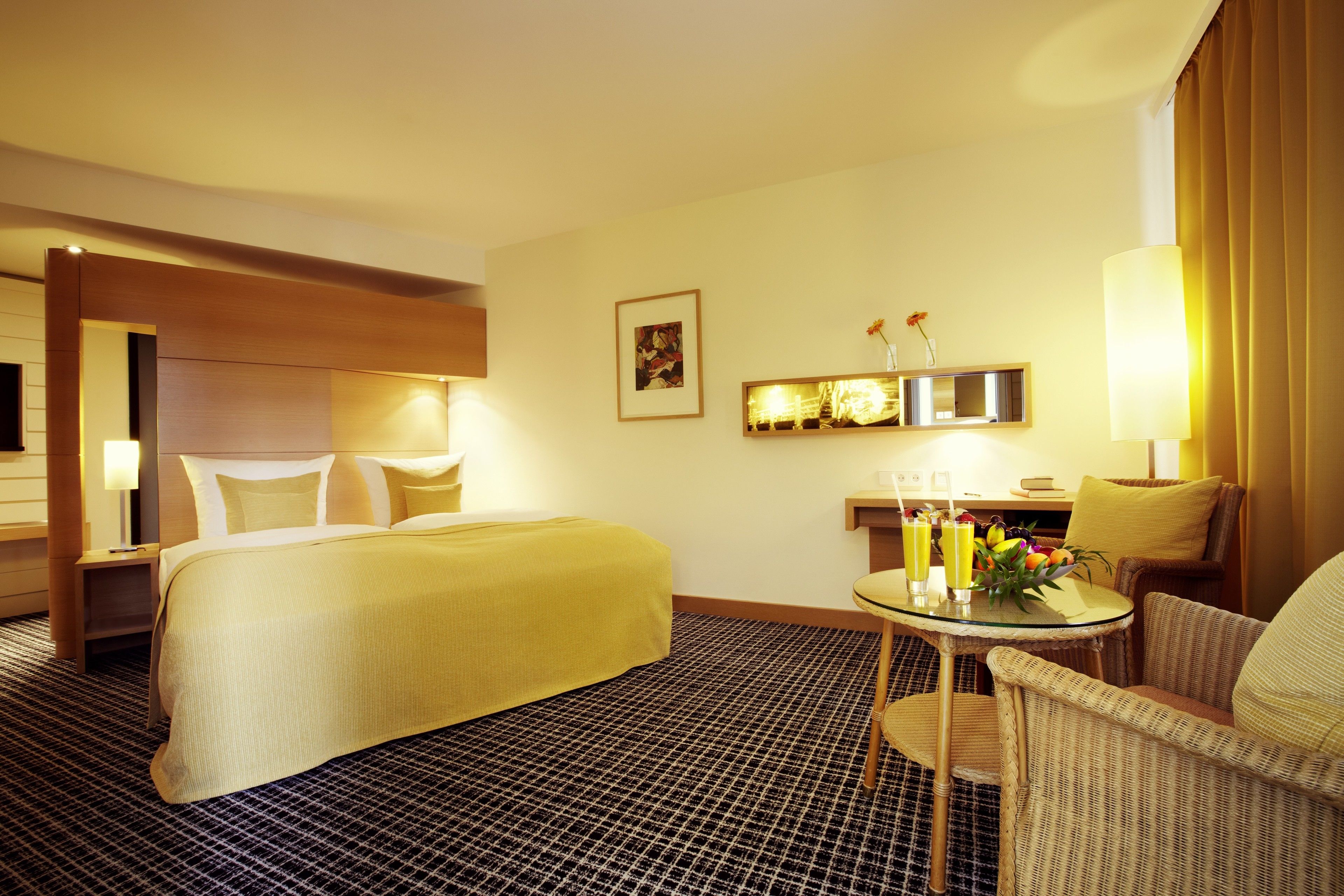 A hotel room with a large bed, a small table with drinks, a chair, and a desk with a lamp.