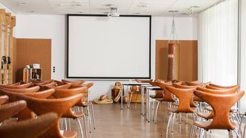 Un salón de conferencias con una pantalla grande, suelo de madera y sillas de cuero marrón.