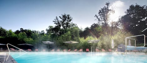 Una piscina techada, una piscina al aire libre, sombrillas