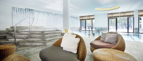 Un área de piscina interior moderna con mobiliario de mimbre, una escalera y vistas a la piscina.