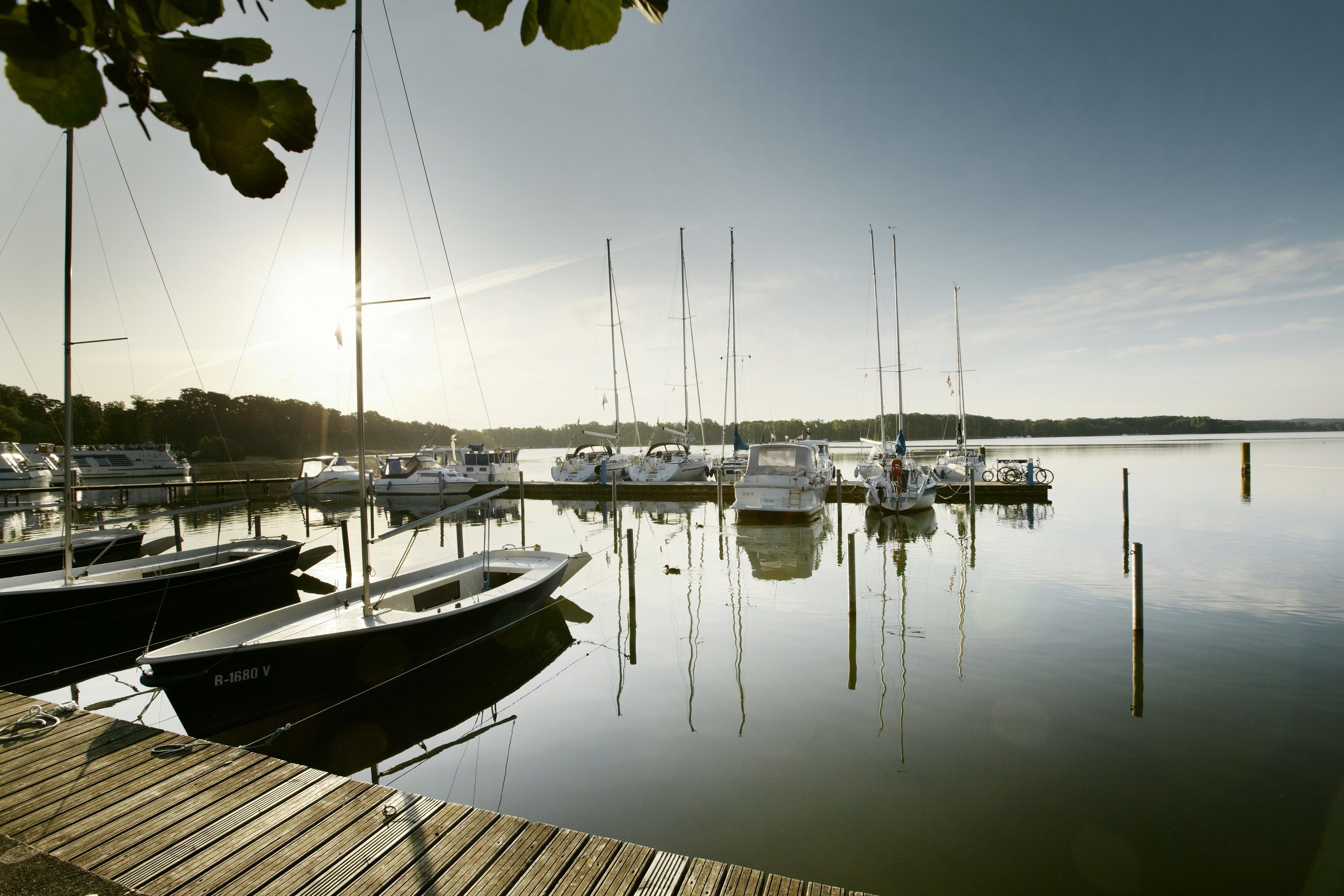 A marina with several boats docked at wooden piers, calm water, and a clear sky.