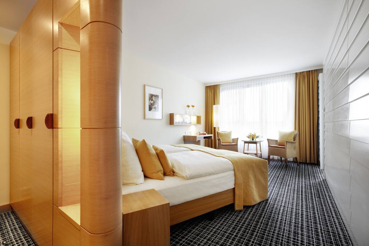A hotel room with a large bed, a desk, a chair, and a window with curtains.