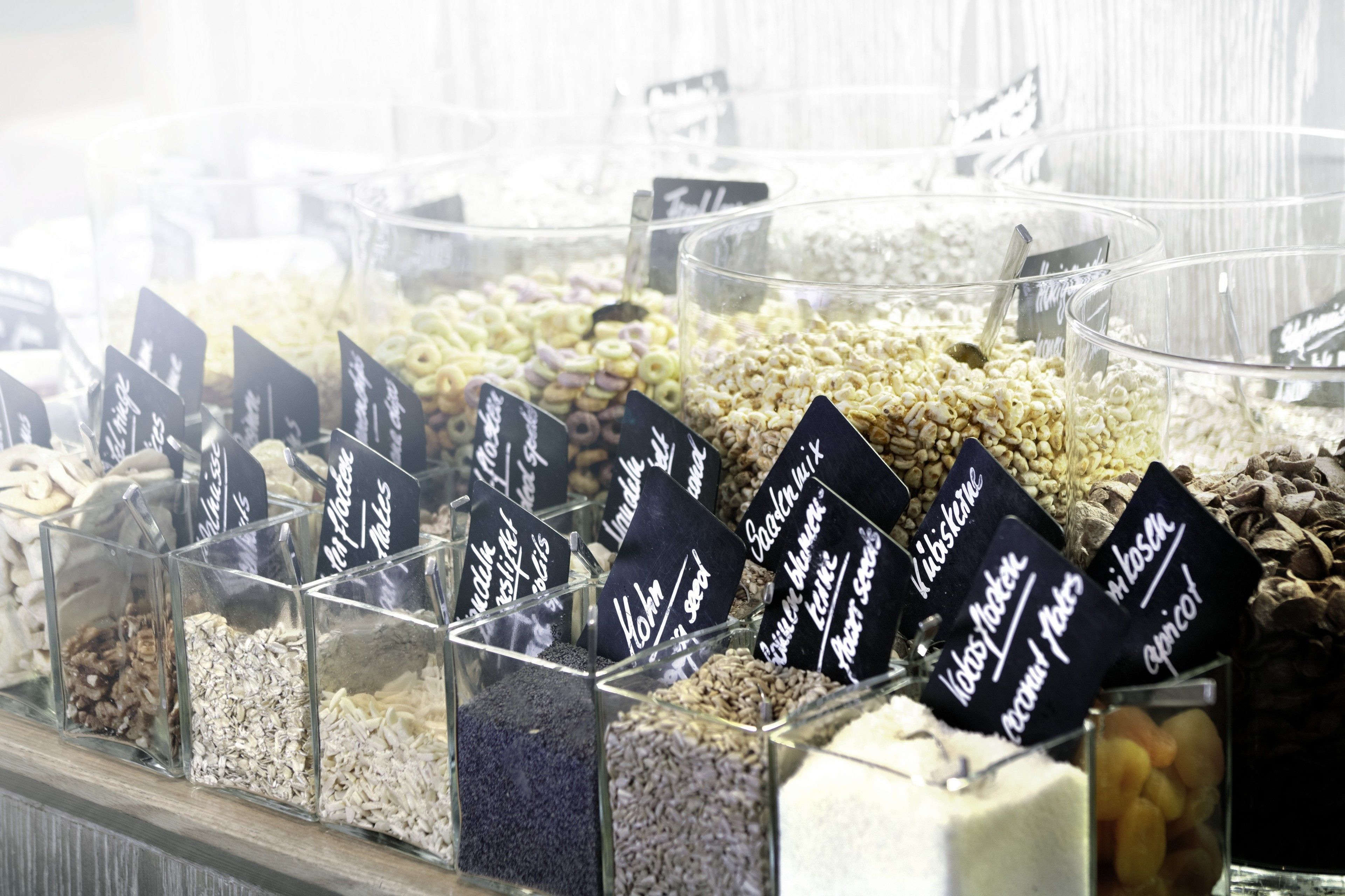 A variety of grains and seeds displayed in clear containers with labels, likely in a store or market setting.