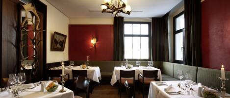 A dining area with tables set for four, a chandelier, a painting on the wall, and a window with curtains.