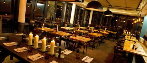 Un restaurante con varias mesas dispuestas para comer, velas en cada mesa y un ambiente cálido y acogedor.