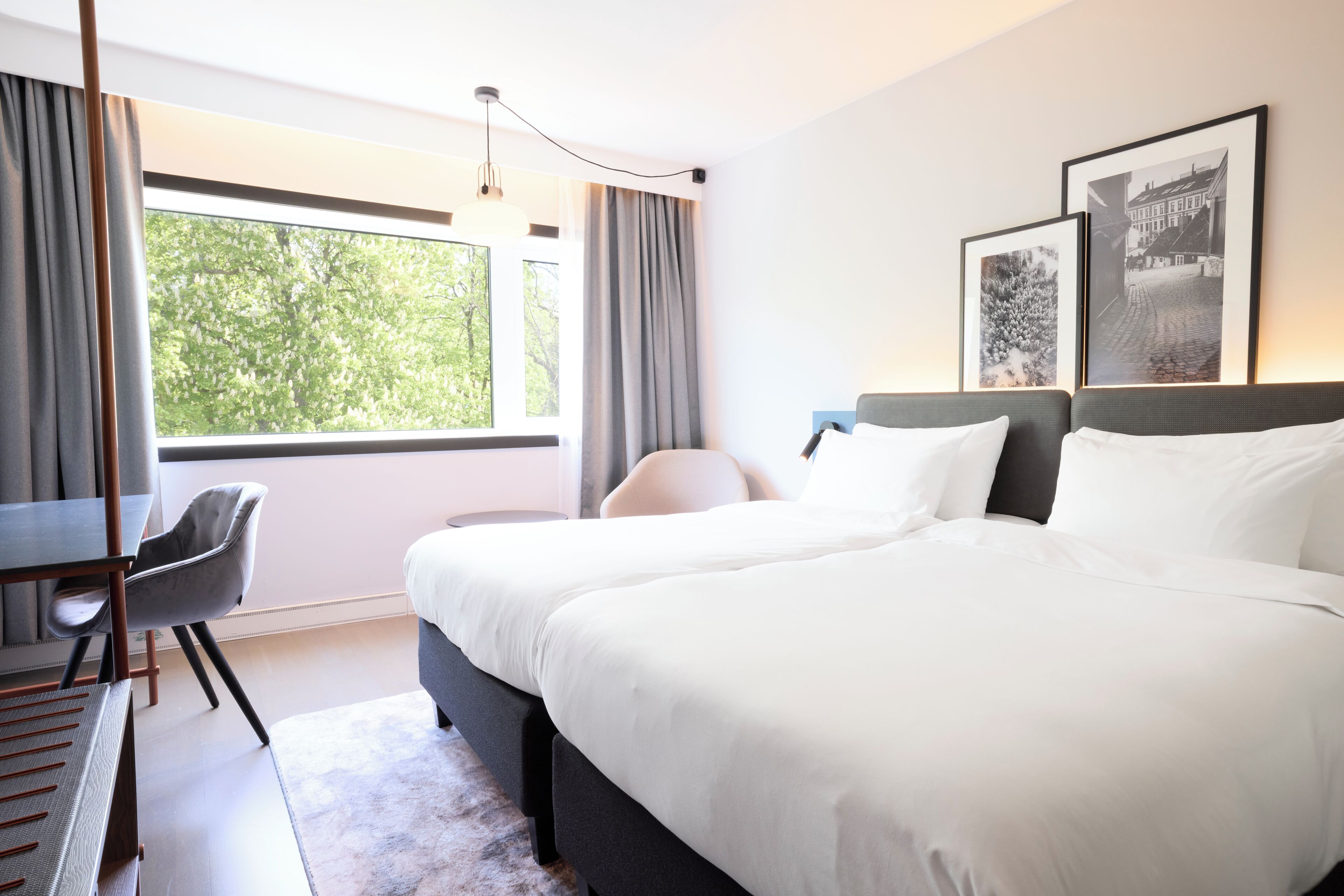 Una habitación de hotel con cama, escritorio, silla y un ventanal grande.