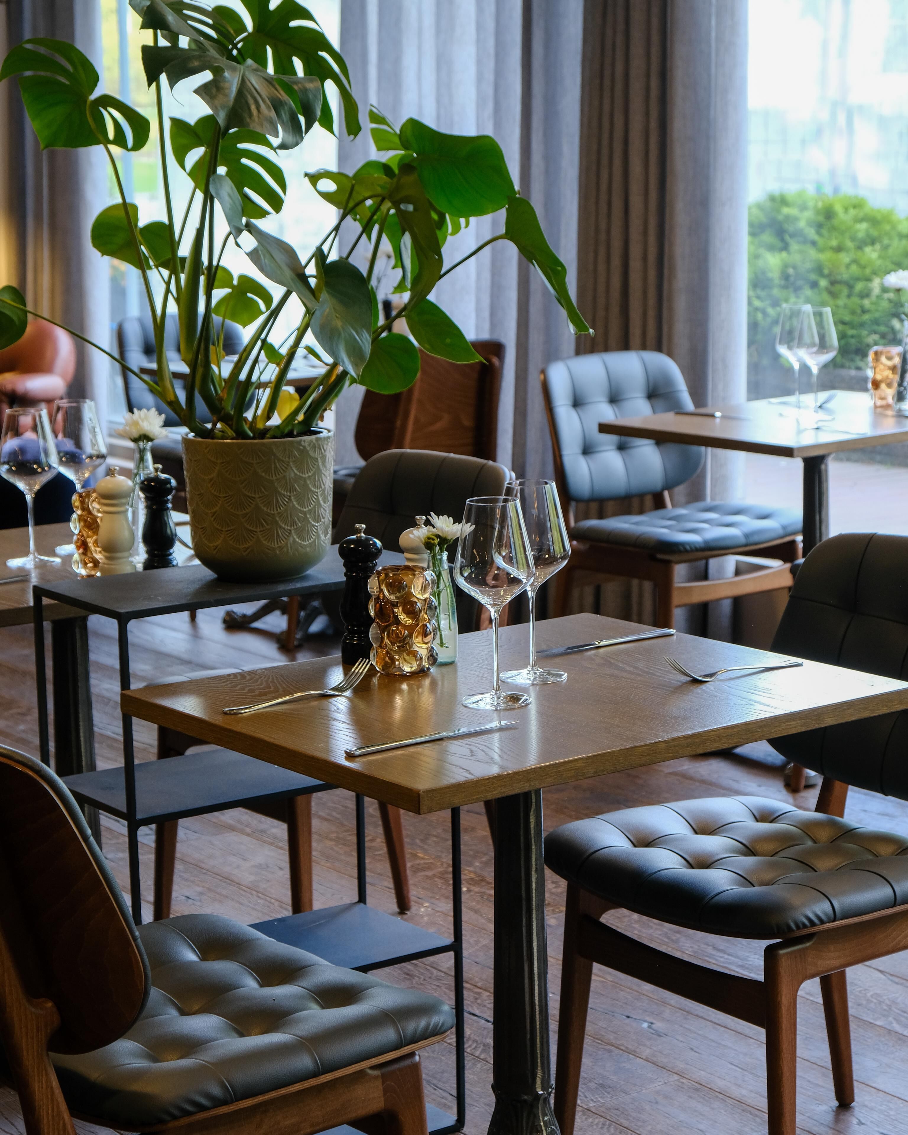 A dining area with a table set for two, a potted plant, and a view of the outdoors.