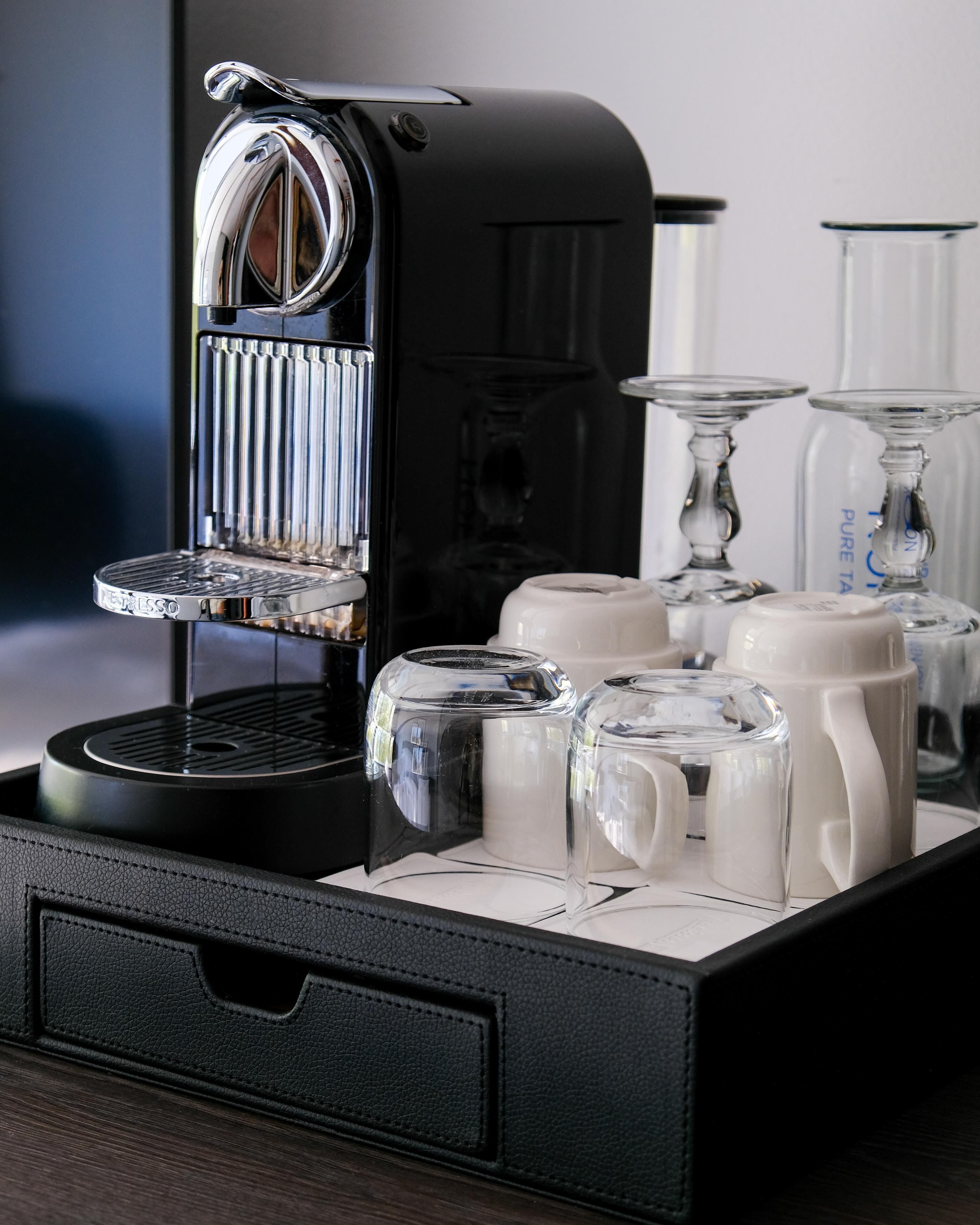 Máquina de café com bandeja, copos de vidro transparente e cafeteira preta.
