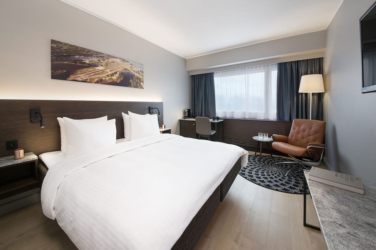 A hotel room with a large bed, a desk, a chair, and a view of a cityscape.