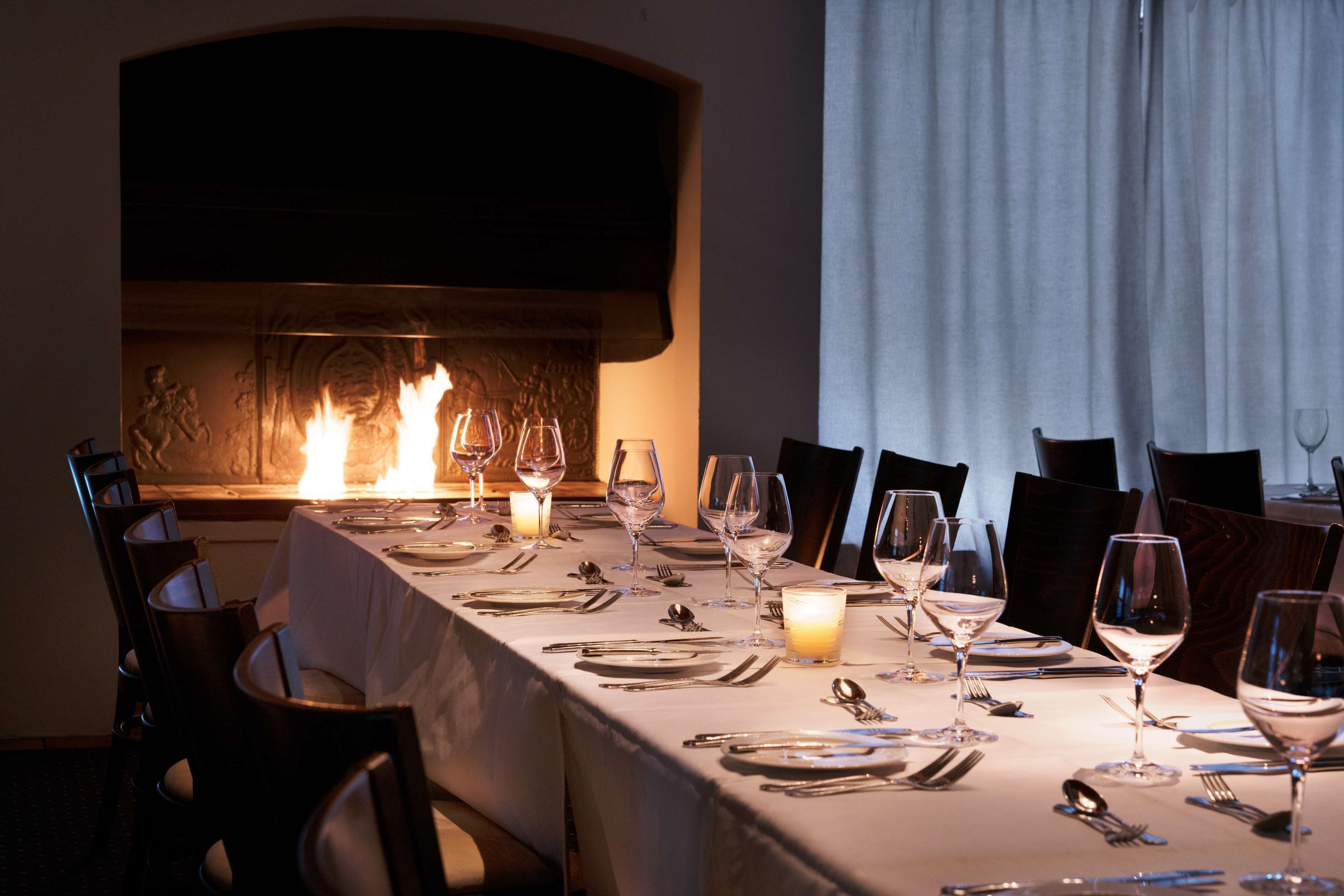 A dining table set for a meal with candles, wine glasses, and cutlery.
