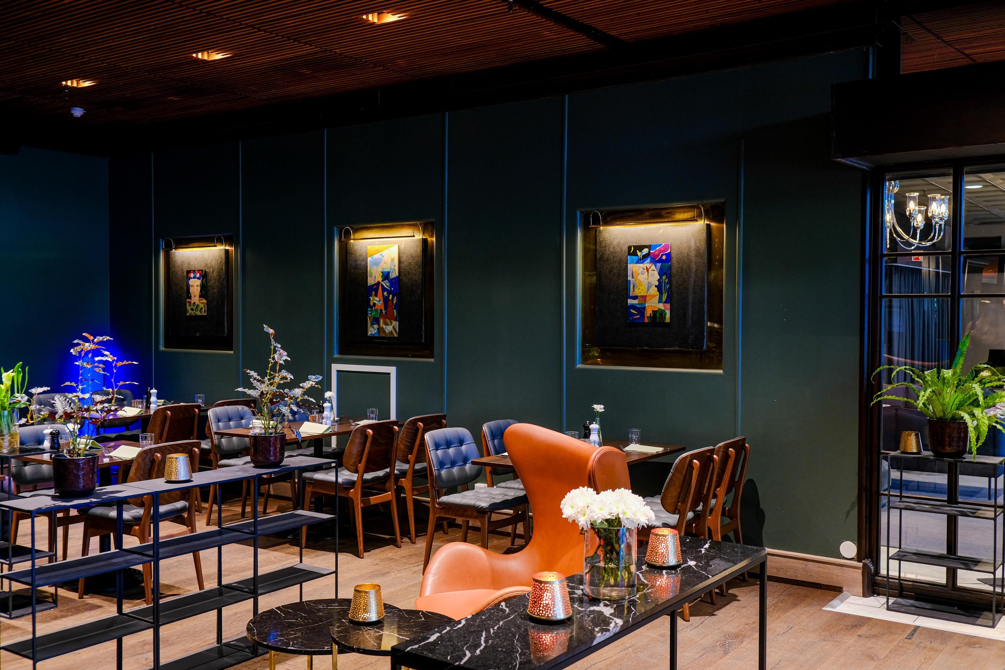 A modern restaurant with dark walls, framed artwork, and a variety of seating including tables and chairs.