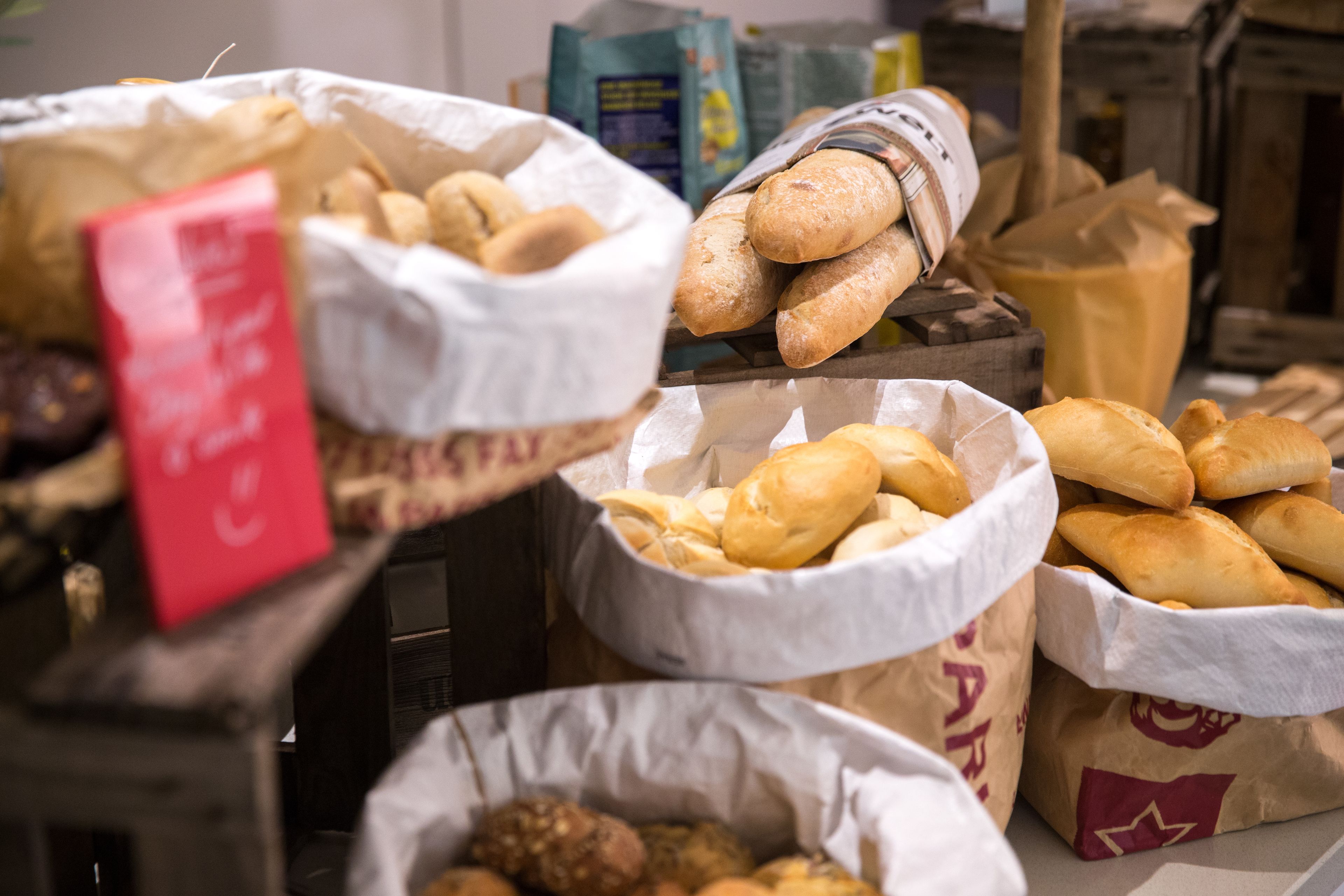 Diversos produtos de panificação expostos em sacos de papel, incluindo pão e pastelaria.