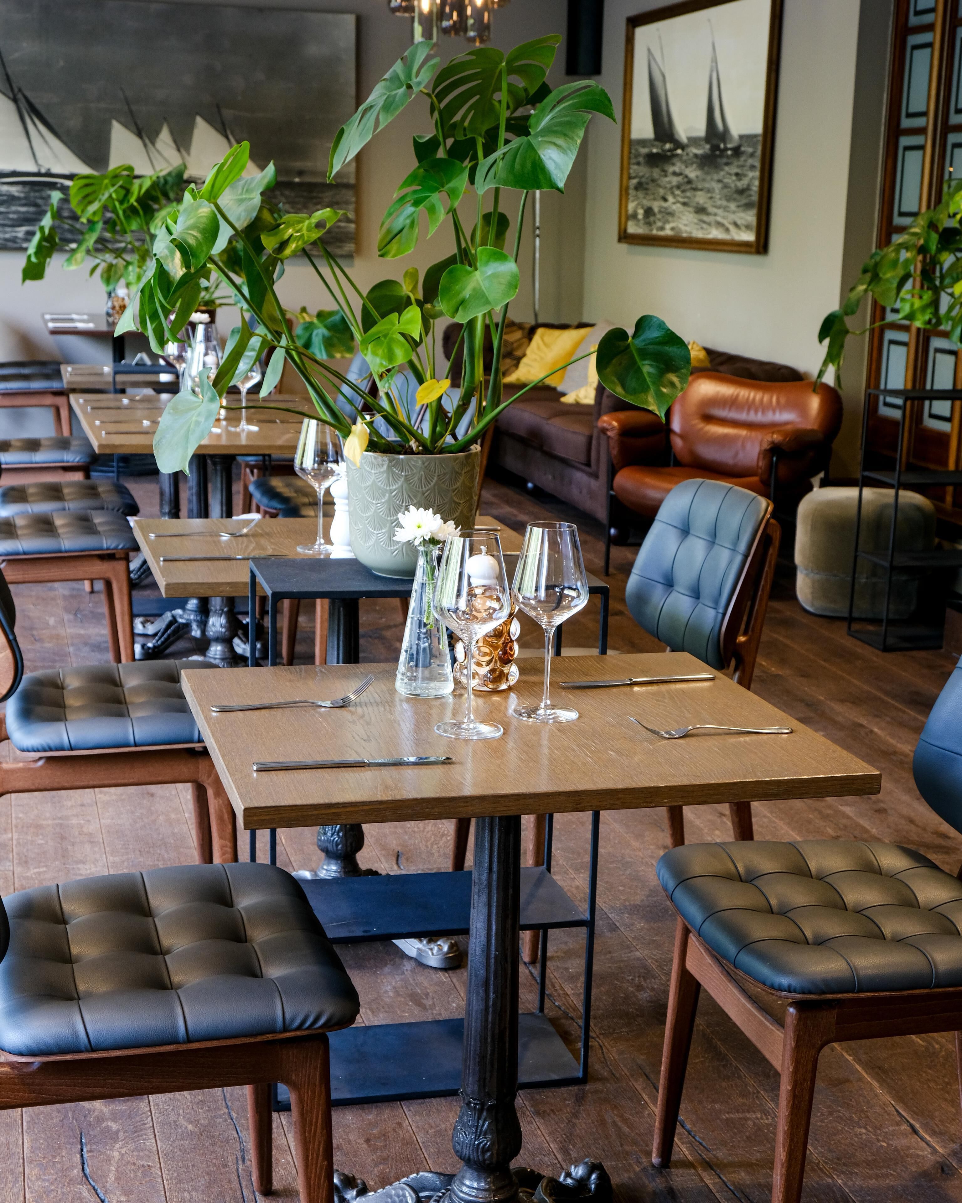 A restaurant interior with wooden tables, leather chairs, and potted plants.