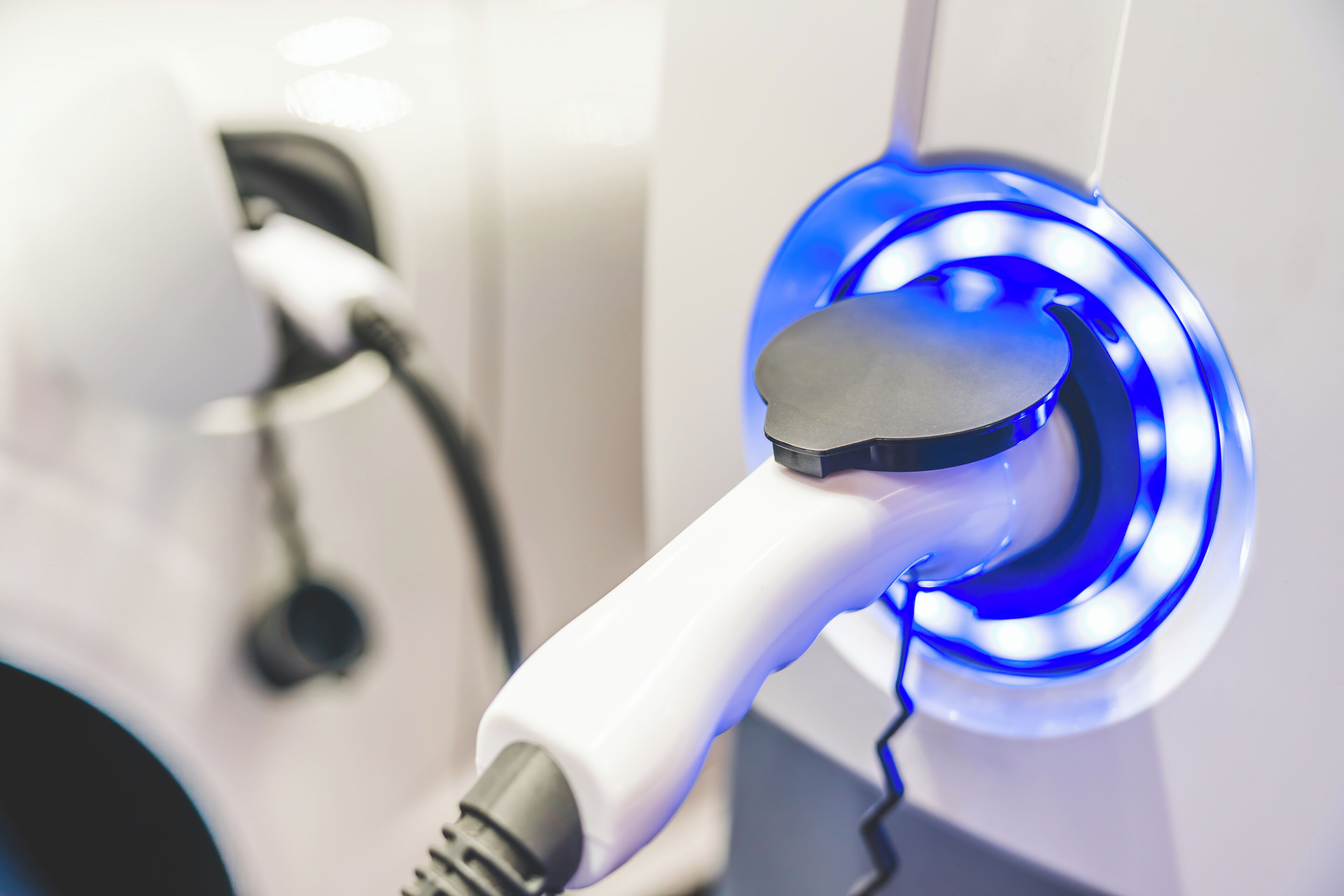 Primer plano de una estación de carga para vehículos eléctricos, con un cable de carga blanco y un puerto de carga azul iluminado.