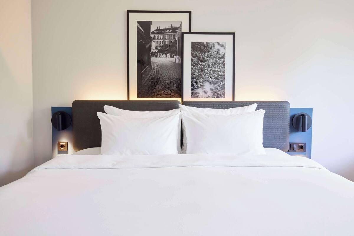 A neatly made bed with white linens, two framed pictures on the wall above, and a modern headboard.