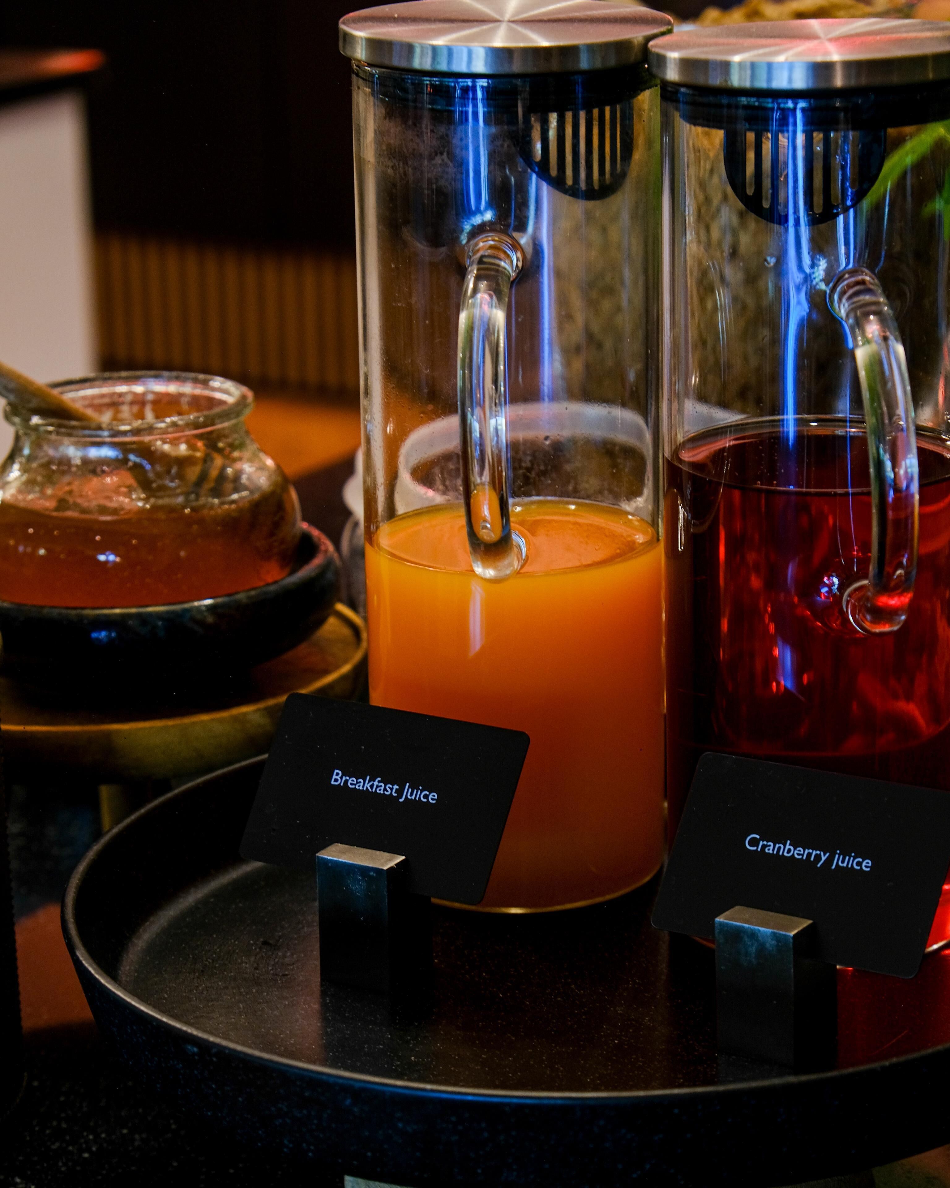 Een ontbijtstation met twee sapdispensers, waarvan één gelabeld 'Breakfast Juice' en de andere 'Cranberry Juice'.