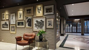 A lobby with a brown leather chair, a small round table with a vase, and a brick wall adorned with framed black-and-white artwork. - Radisson Blu Park Hotel, Oslo (Bærum)