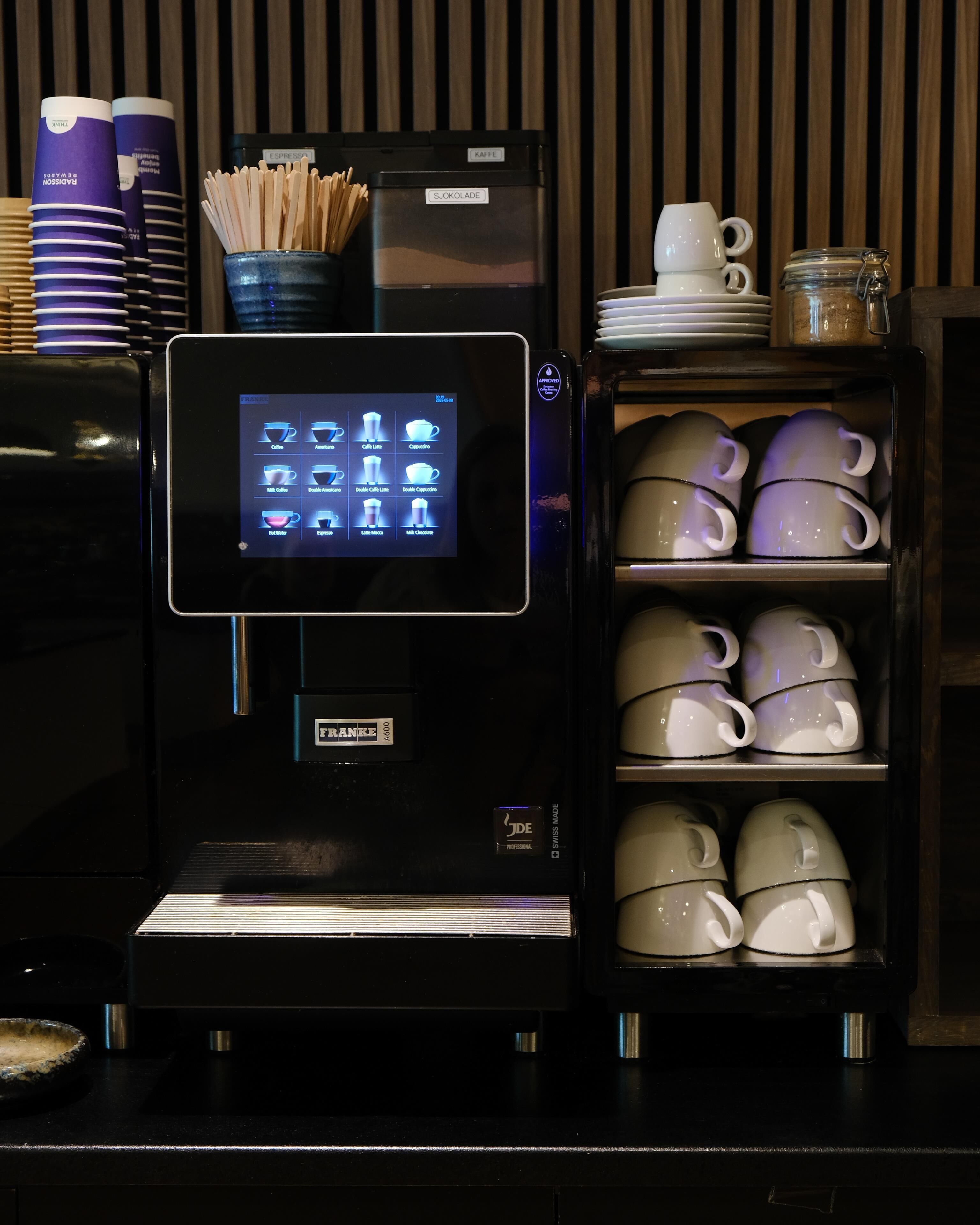 Une machine à café dotée d’un écran numérique, d’un porte-tasse et d’une étagère où sont empilées les tasses.