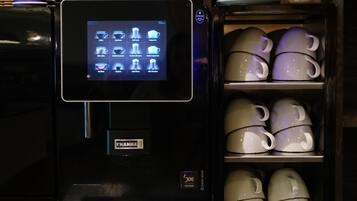 Une machine à café dotée d’un écran numérique, d’un porte-tasse et d’une étagère où sont empilées les tasses.