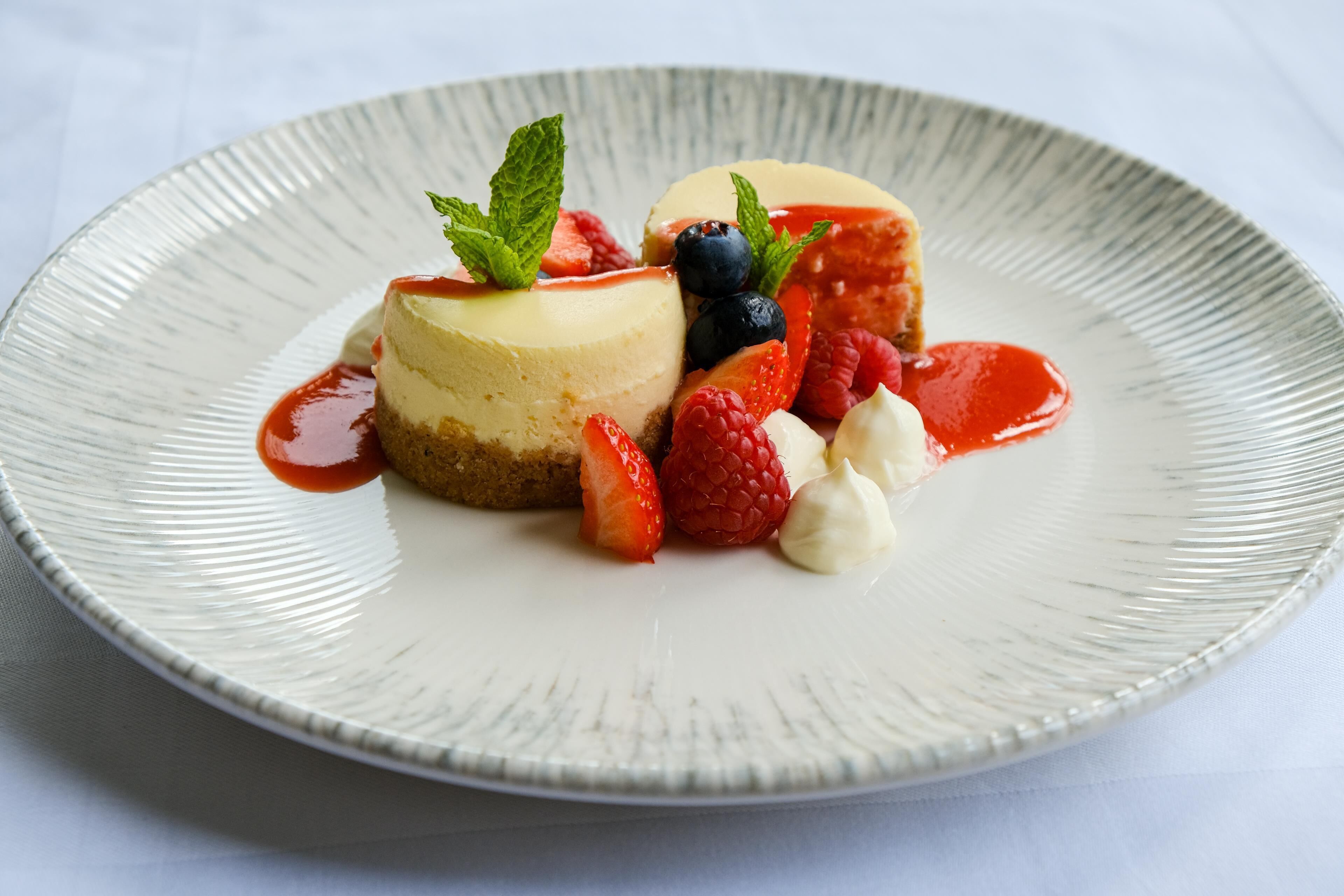 A dessert plate with a cheesecake, strawberries, raspberries, and a mint garnish.