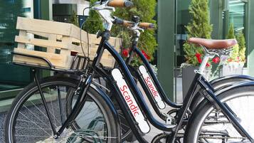 Una bicicleta con una caja de madera en el frente, estacionada frente a un edificio de ventanas de vidrio y plantas en macetas.