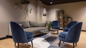 Una sala moderna con un sofá gris, dos sillones azules, una mesa de centro y una estantería con plantas.