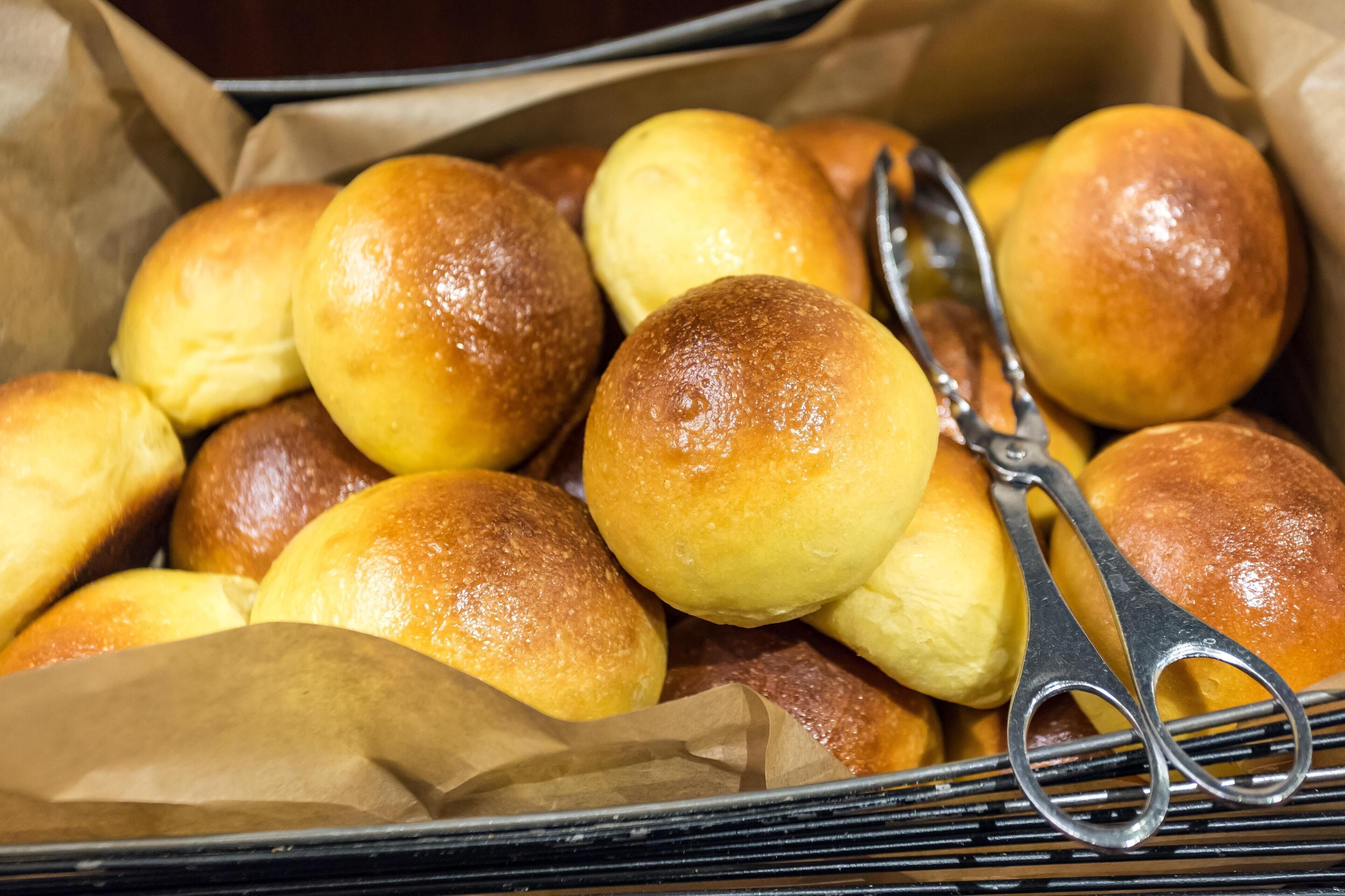 A tray of freshly baked rolls with a pair of tongs resting on top.
