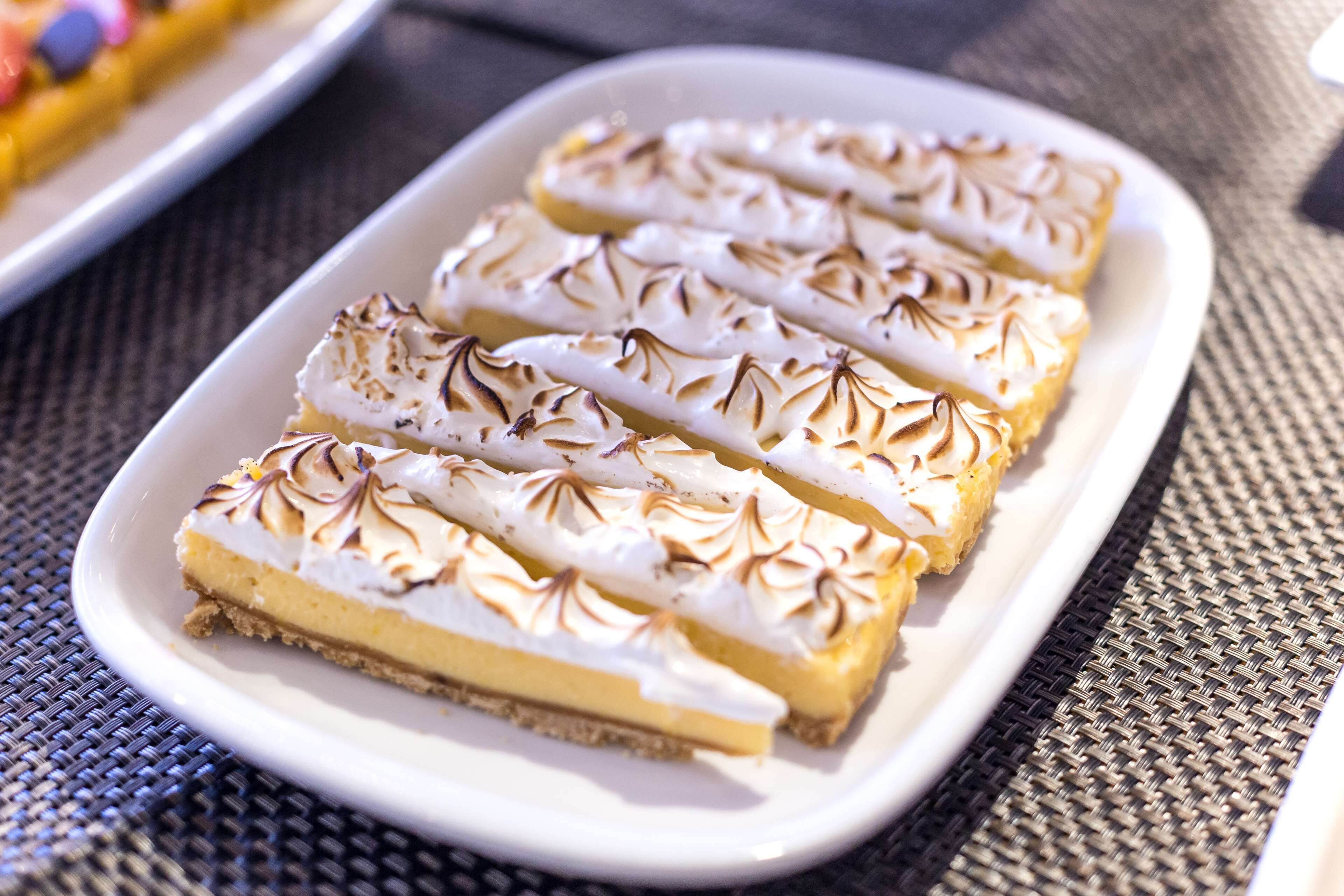 A white rectangular plate with four slices of a layered dessert, possibly a pie or tart, on a woven tablecloth.