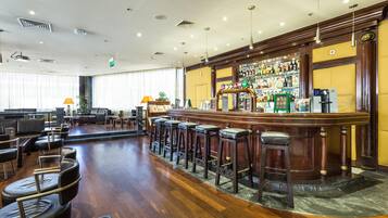 Zona de bar con taburetes, barra y área de estar con mesas y sillas.