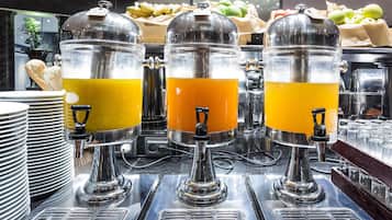 A buffet setup with three beverage dispensers, a fruit display, and stacked plates.