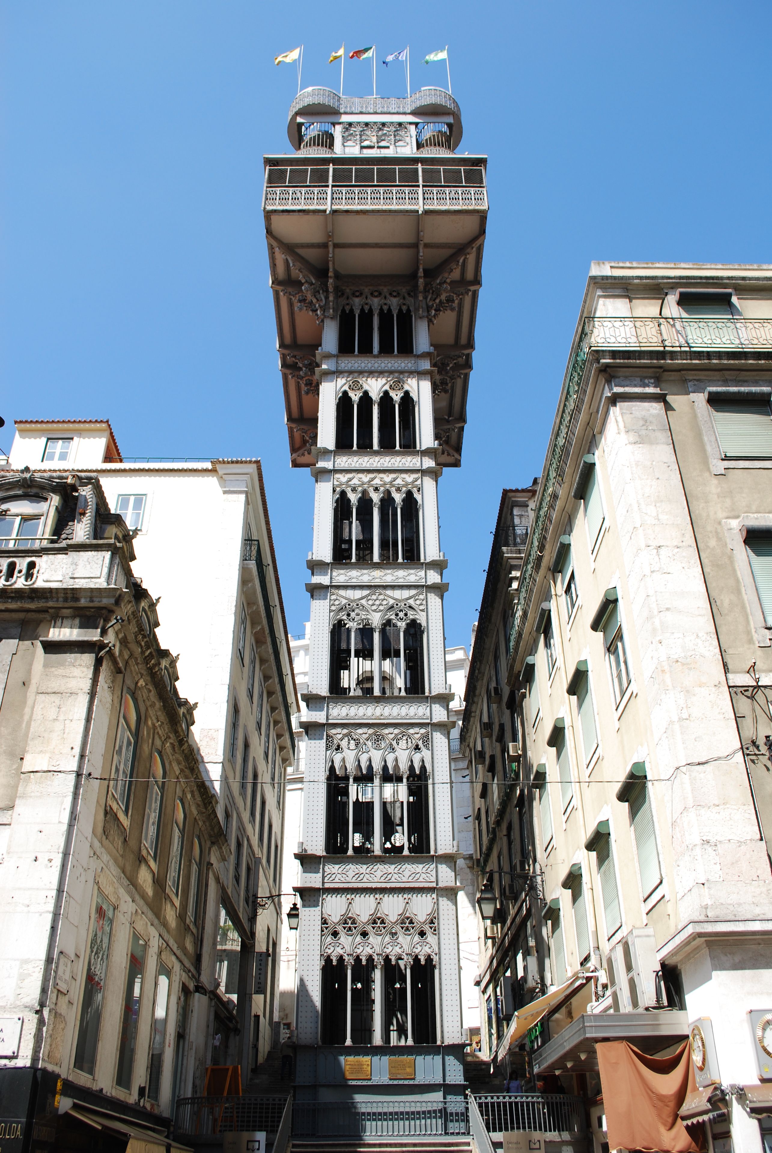 A historic building with a central tower featuring ornate architectural details and multiple flags.