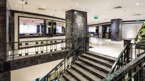 Un moderno vestíbulo de hotel con suelo de mármol, una escalera central y una zona de recepción.
