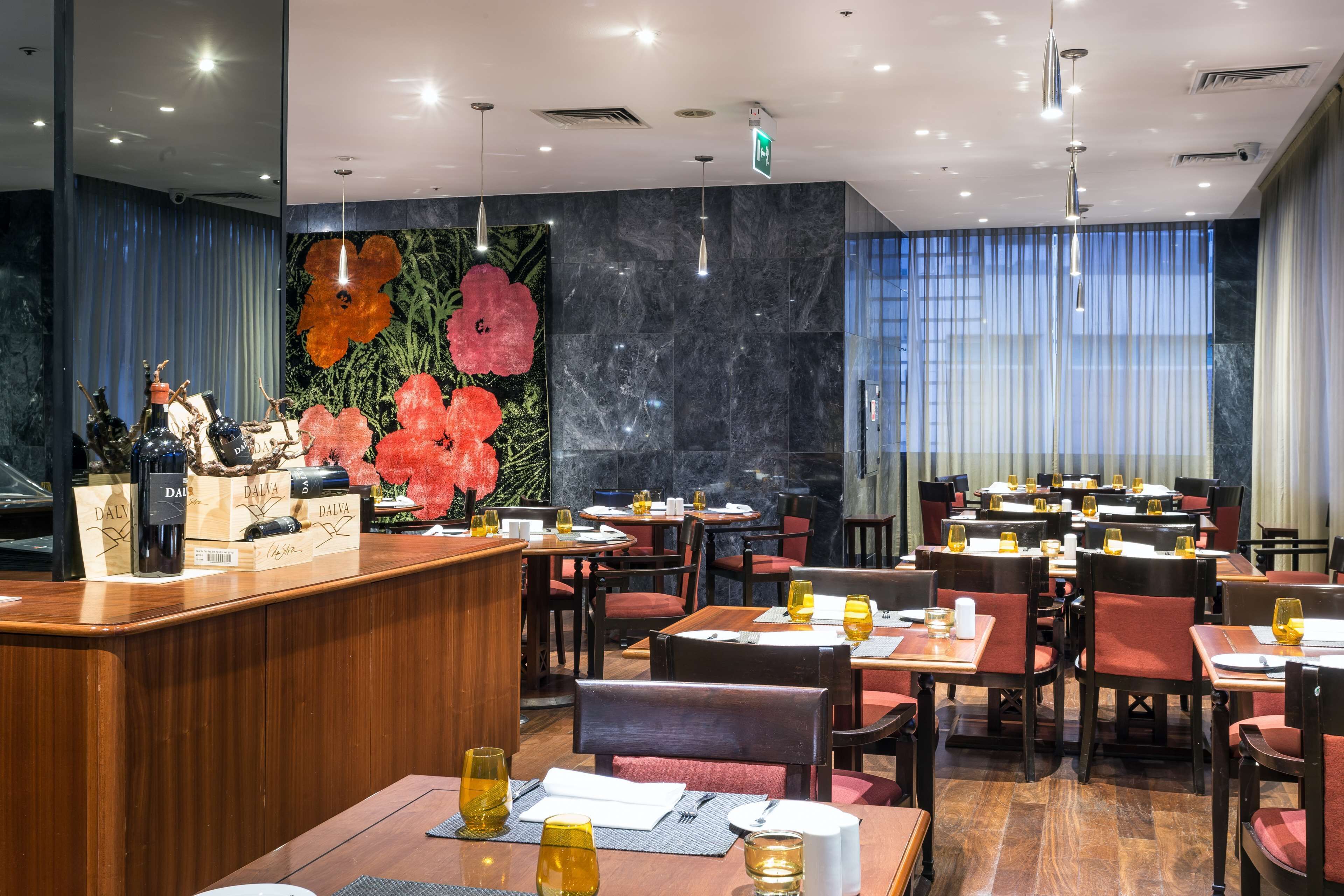 A restaurant with marble walls, wooden furniture, and a large floral mural. Tables are set with glasses and cutlery.