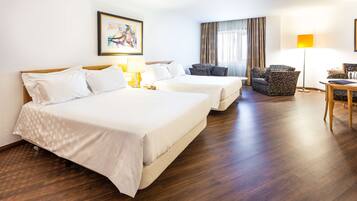 A hotel room with two beds, a desk, a chair, a lamp, and a painting on the wall.