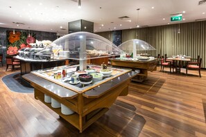A buffet setup with multiple serving stations, a wooden floor, and a green exit sign. - Radisson Blu Hotel (Lisbon)